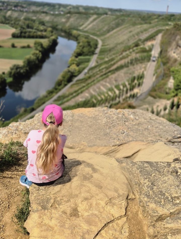 Sophie sitzt auf einem Felsen und schaut über Fluss und Weinberge
