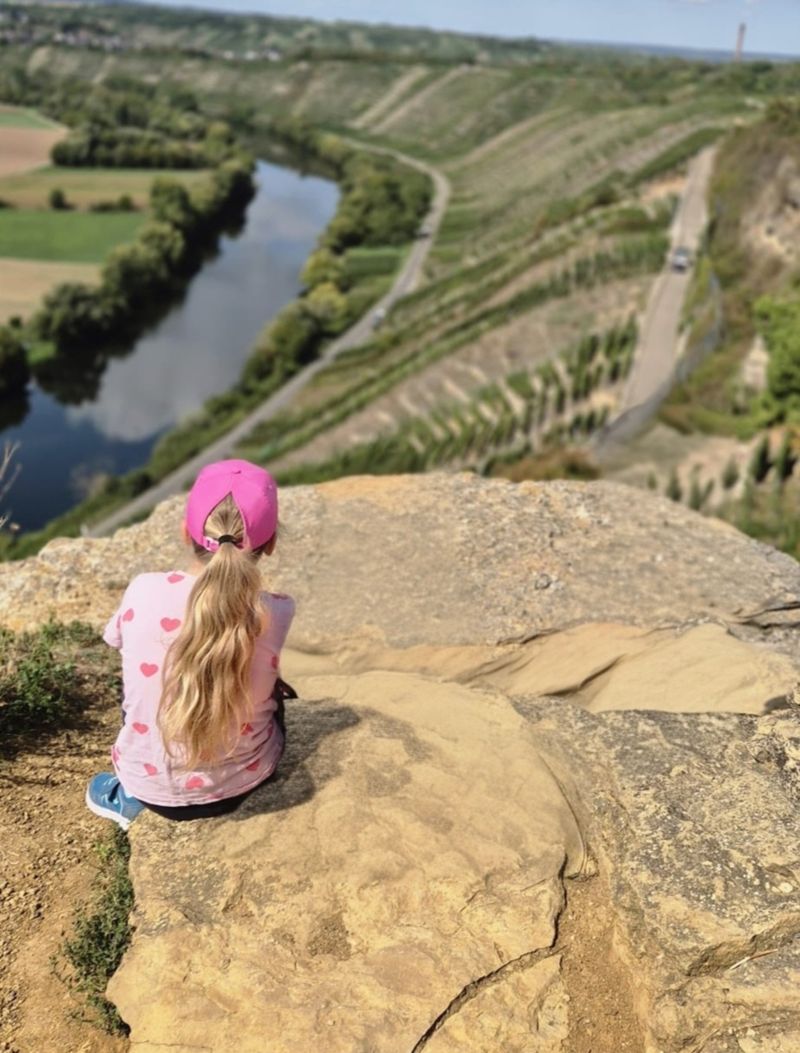 Sophie sitzt auf einem Felsen und schaut über Fluss und Weinberge